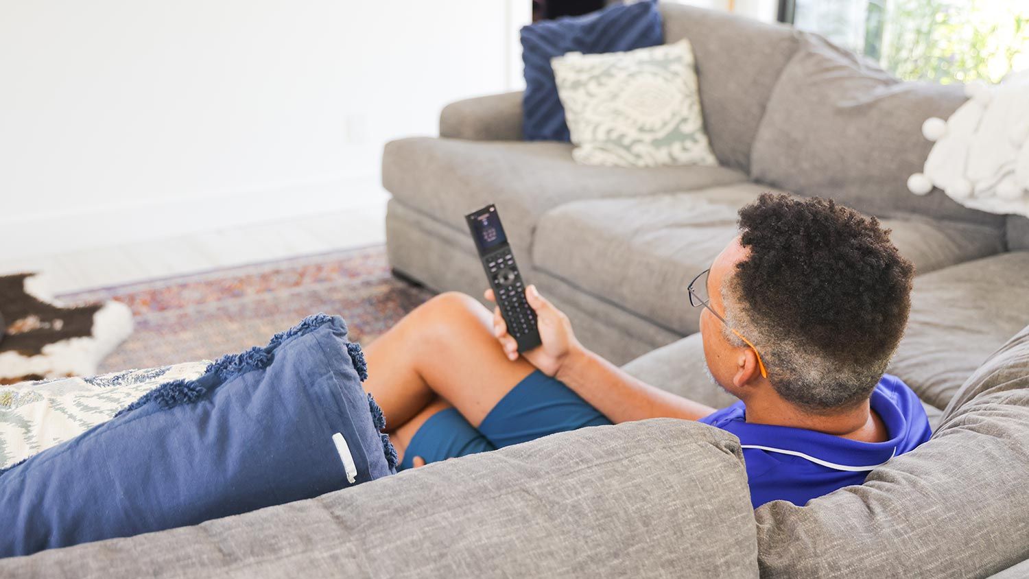 A person sitting comfortably on a sofa, holding a remote control to adjust audio or video settings.