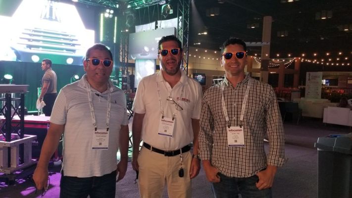 Three people wearing sunglasses and laughing at a convention.