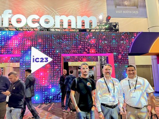 Three men posing in front of a brightly lit entrance at a tech event.