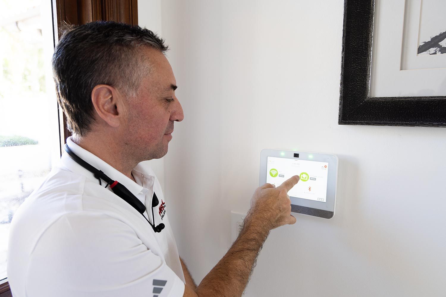 A man pressing buttons on a white wall-mounted security alarm keypad.