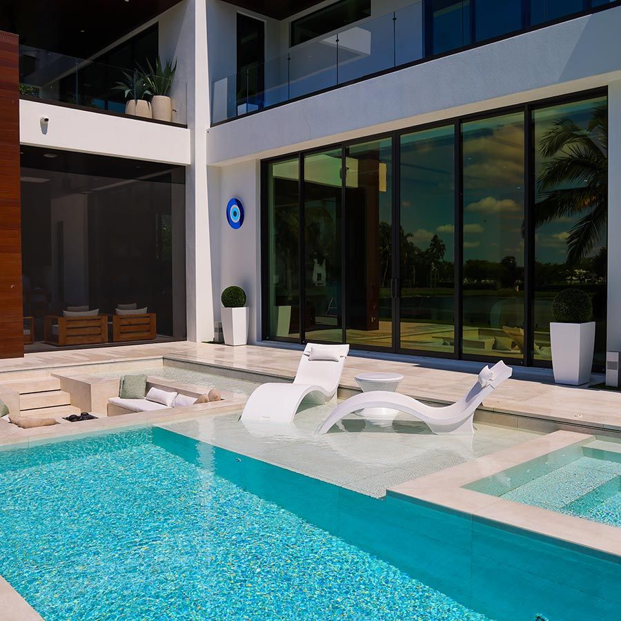 Modern outdoor pool area with lounge chairs, glass sliding doors, and landscaped surroundings.