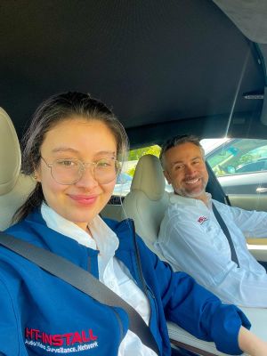 A smiling duo taking a selfie in a car, both wearing uniforms and seated in the front seats.