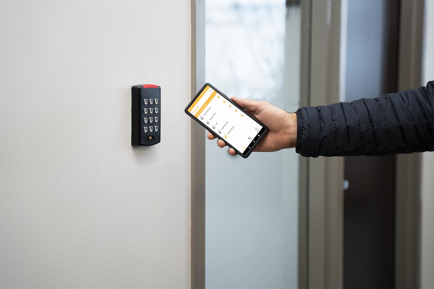 A person using a smartphone to interact with a wall-mounted access control keypad.