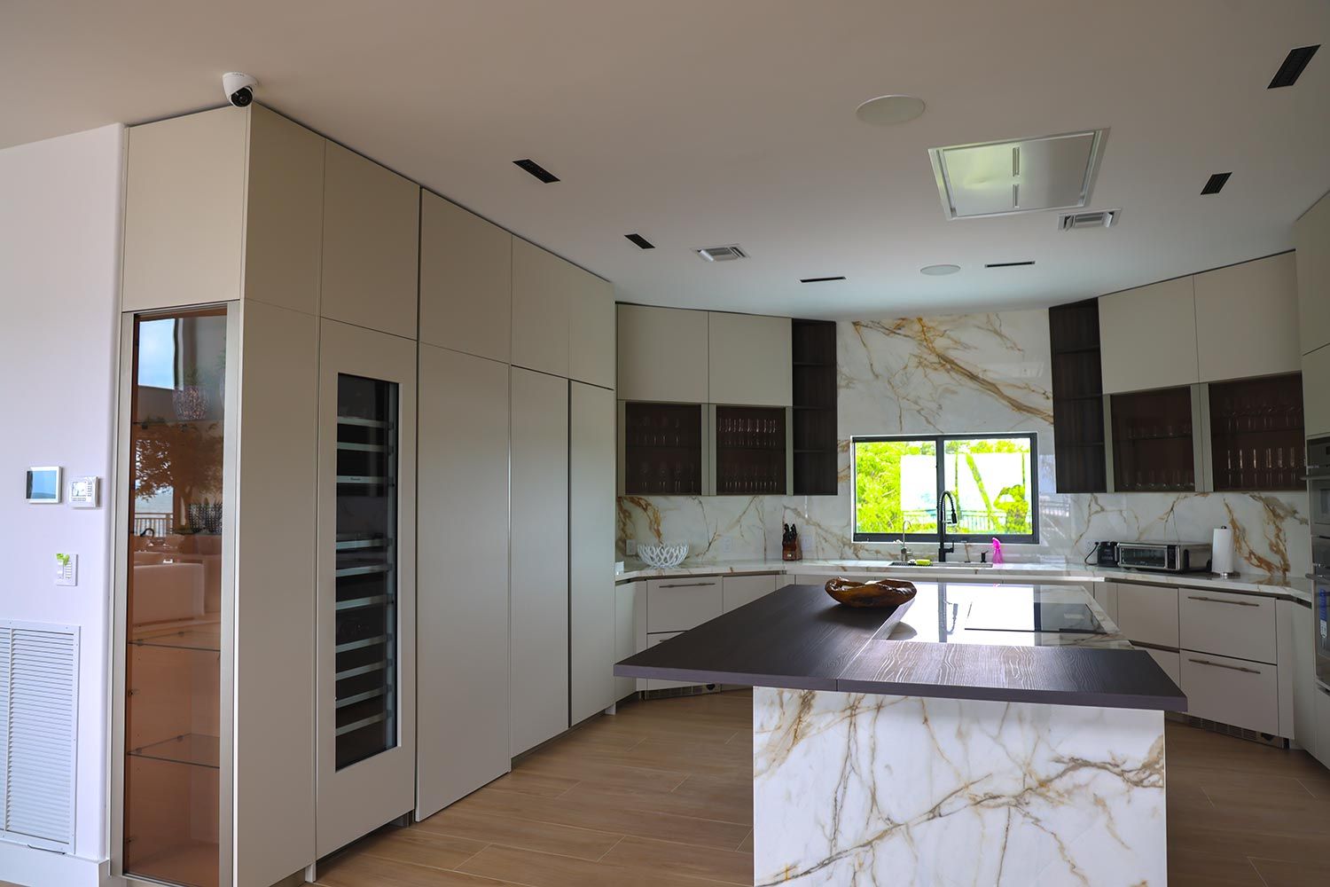 A modern kitchen with marble finishes, integrated appliances, and a discreet ceiling camera.