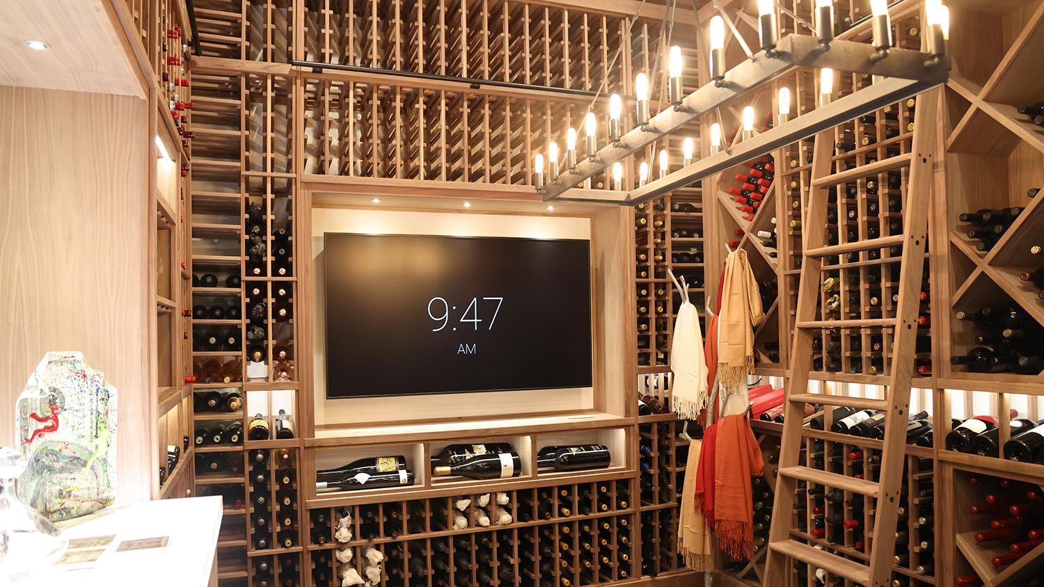 A modern wine cellar with a large digital display and wooden racks filled with bottles of wine.