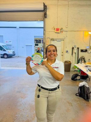 A team member standing in a workshop, smiling and holding a playful award plate.