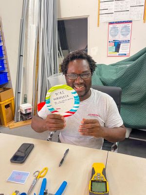 A team member sitting at a table, smiling and holding a colorful award plate in a workshop.