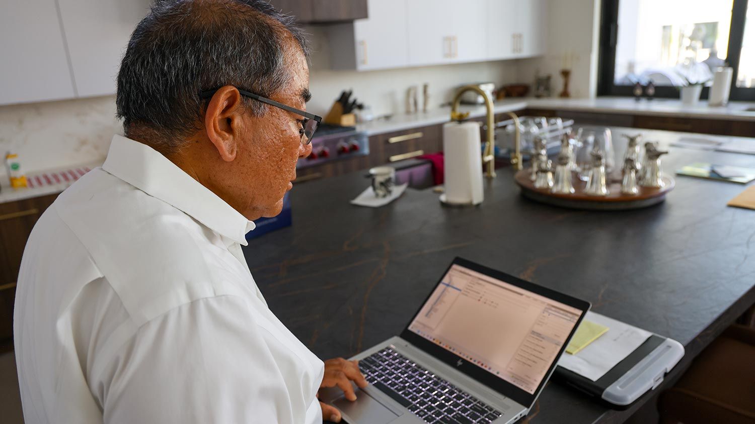 A man using a laptop at a kitchen counter, programming or working on a technical system interface.