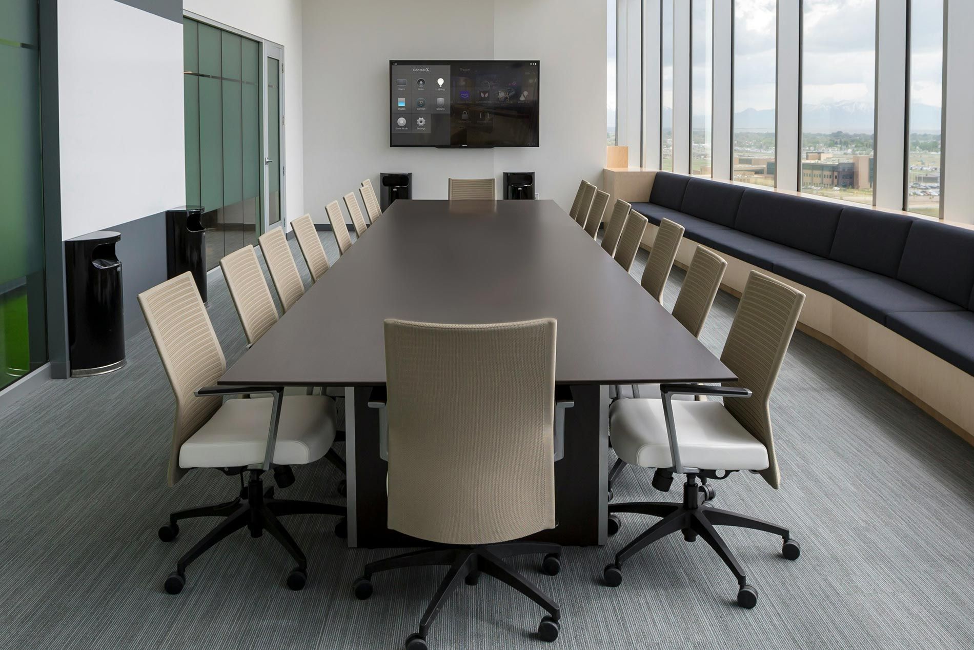 A contemporary conference room with a large table, chairs, and a wall-mounted control display.