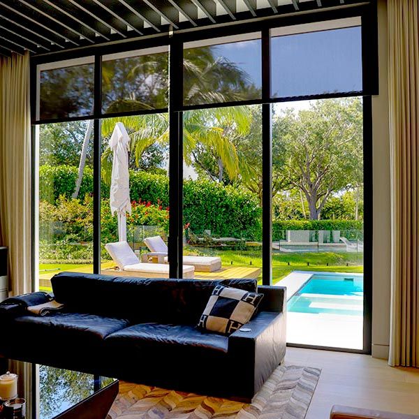 Living room view with large glass windows showcasing a backyard pool and greenery, accompanied by motorized blinds.