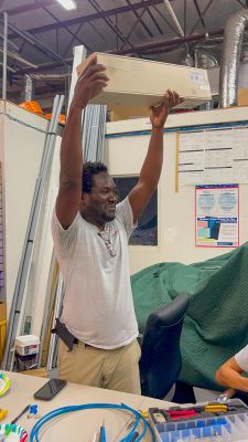 A person happily raising a box over their head in an office workshop setting.