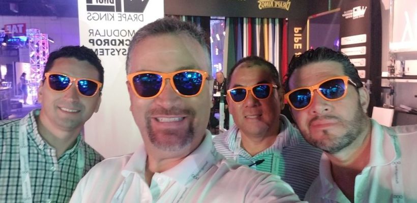 A group of four men wearing sunglasses and smiling for a selfie at an event.