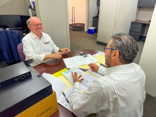 Two professionals discussing project plans at a table with papers and equipment around.