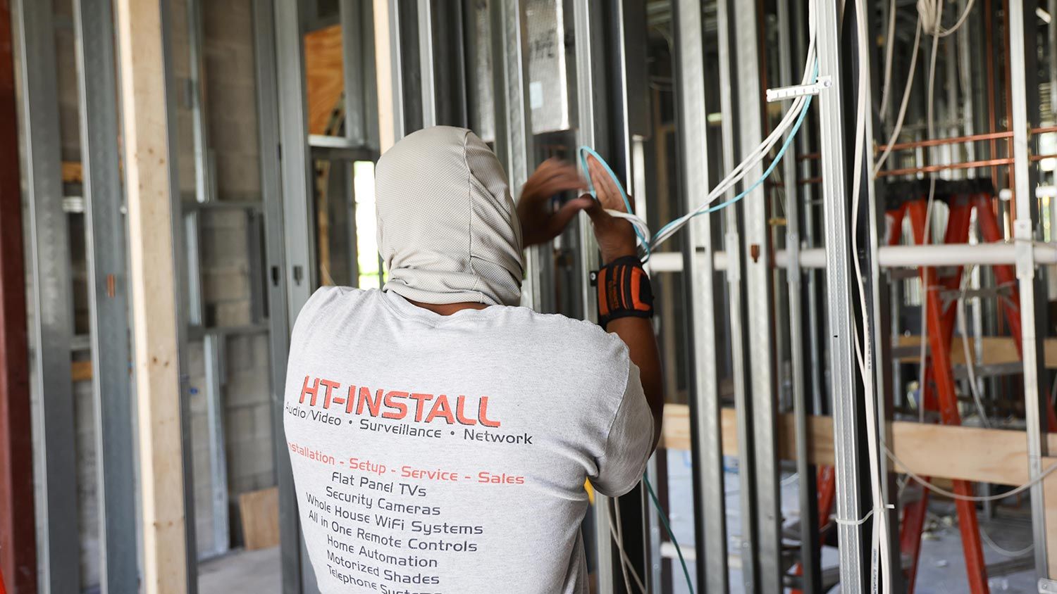 A technician wearing a hood installing wiring into the framing of a building under construction.