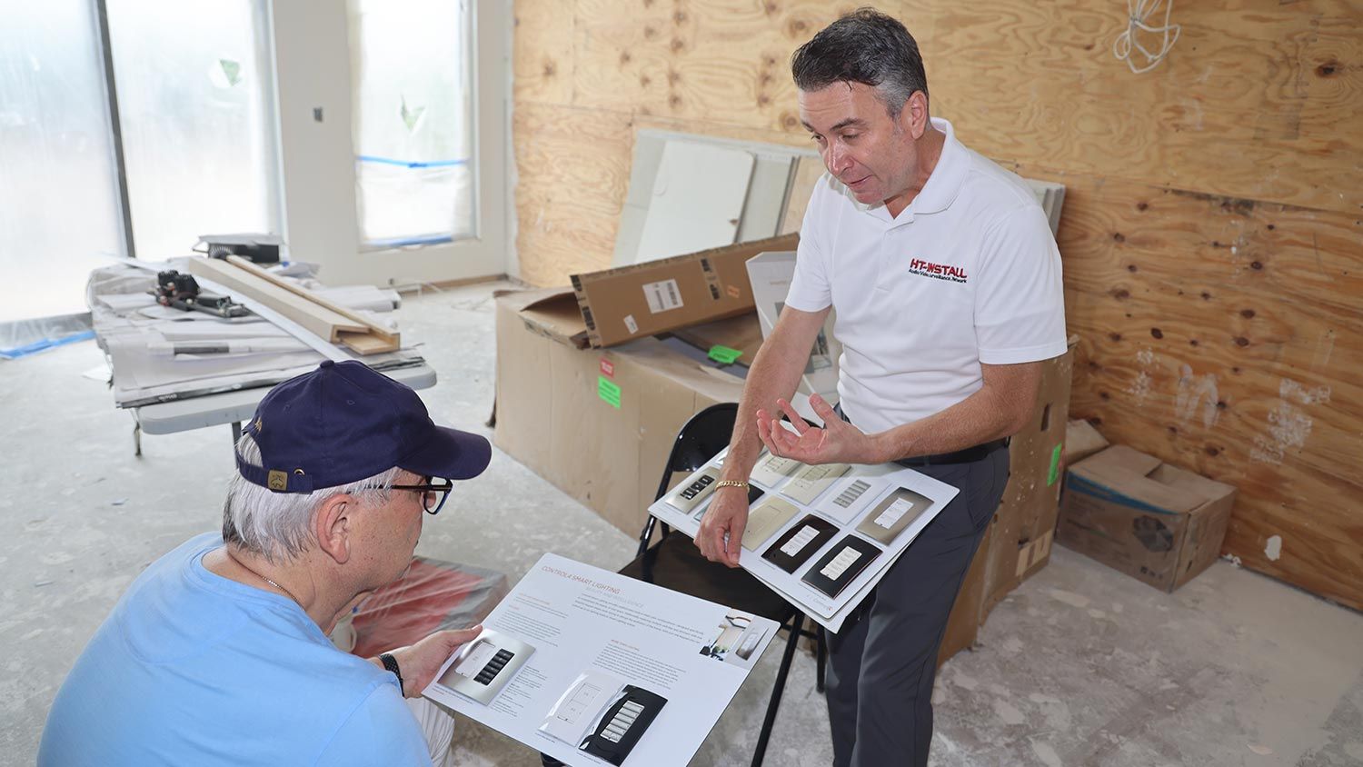 A technician explaining various options to a client using a catalog of switches in a construction setting.