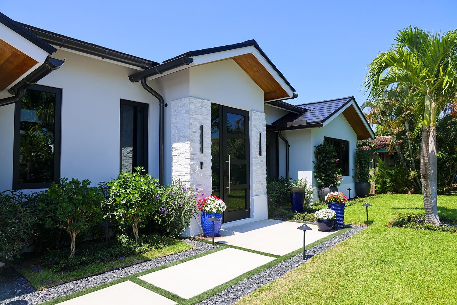 A contemporary home entrance with a stone facade, pathway lighting, and lush landscaping.